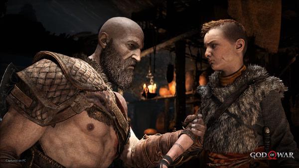 Screenshot from God of War showing a muscular, armored character shaking hands with a young person in a fur-lined outfit inside a dimly lit room.