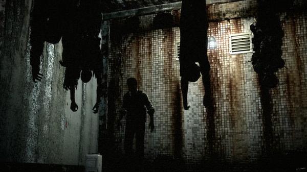 A screenshot from The Evil Within showing a dark, grimy room with hanging corpses and a silhouetted figure walking below.