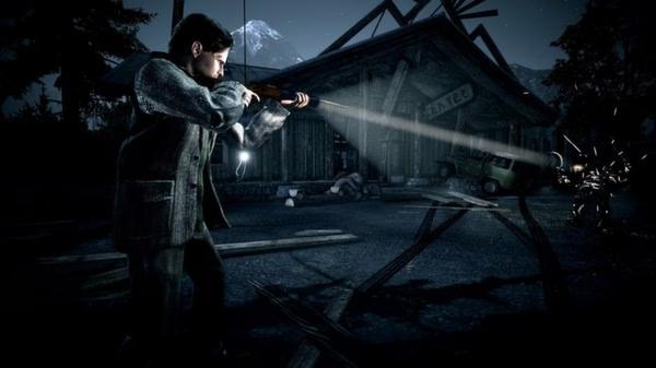 Alan Wake screenshot: A man shines a flashlight and points a shotgun in a dark, eerie setting with a wooden building in the background.