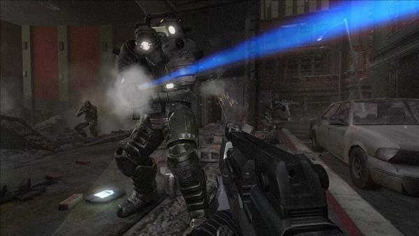 F.E.A.R. 2: Project Origin screenshot showing a player aiming at an armored enemy in a war-torn urban setting with debris and a car.