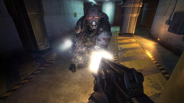 Screenshot from F.E.A.R. 2: Project Origin showing a player aiming a weapon at an armored enemy in a dimly lit corridor.