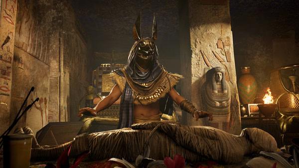 Screenshot from Assassin's Creed Origins showing a masked figure resembling Anubis with a mummy in an ancient Egyptian tomb.