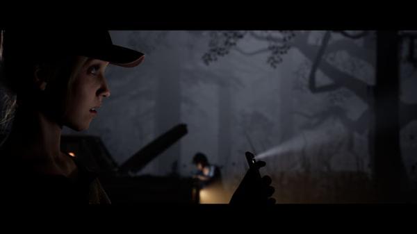 The Quarry screenshot: A person in a cap holding a phone in a dark forest, with another person near a car in the background.