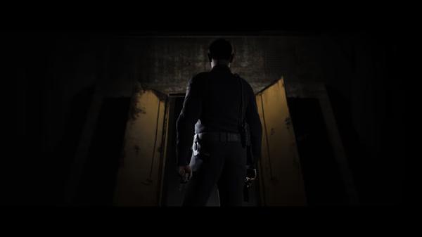 Screenshot from The Quarry showing a lone character standing in a dark room, facing an open door with dim lighting.