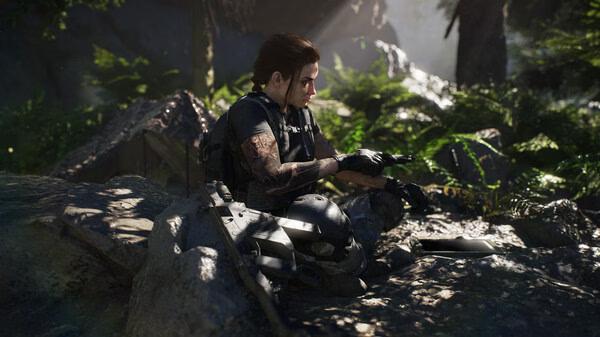 A character sits on a rock in a forest in Tom Clancy's Ghost Recon Breakpoint screenshot, wearing tactical gear.