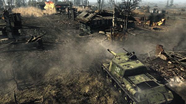 Screenshot from Call to Arms - Gates of Hell: Ostfront showing a tank advancing through a war-torn village, surrounded by smoke and debris.