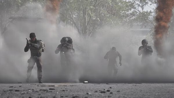 WARDOGS screenshot: Four armed soldiers emerge from dense smoke on a battlefield, with orange plumes rising in the background.
