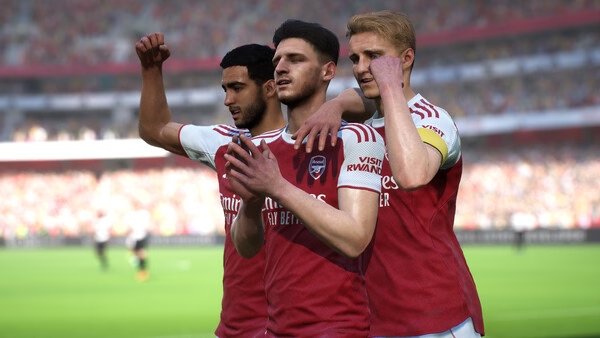 eFootball™ screenshot showing three soccer players in red and white jerseys celebrating on a vibrant, crowded stadium field.