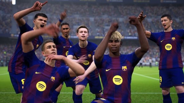 A team of players celebrates a goal in a stadium in an eFootball™ game screenshot, wearing blue and red jerseys.
