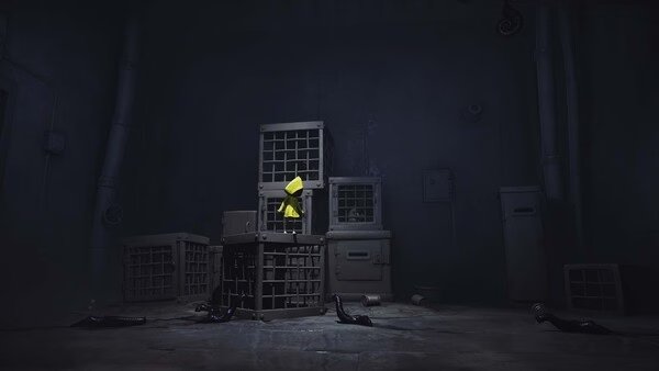 Little Nightmares screenshot: A small figure in a yellow raincoat stands on a stack of cages in a dimly lit, eerie room.