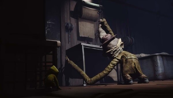 Screenshot of Little Nightmares showing a small character in a yellow raincoat hiding from a tall, lurking creature in a dimly lit room.