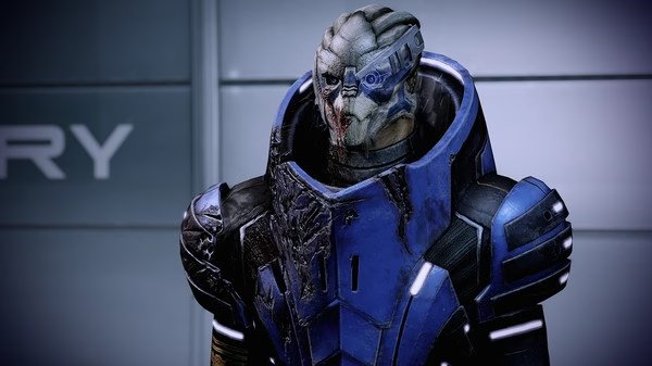 Mass Effect™ Legendary Edition screenshot: A character in blue armor stands against a gray wall, displaying a futuristic design.