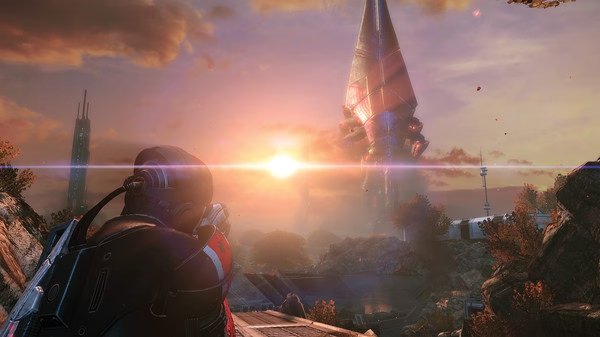 A screenshot from Mass Effect™ Legendary Edition shows a soldier gazing at a towering structure during a vibrant sunset.