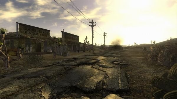 Screenshot from Fallout: New Vegas. A cracked road leads to buildings under a vast sky in the desolate town of Goodsprings.