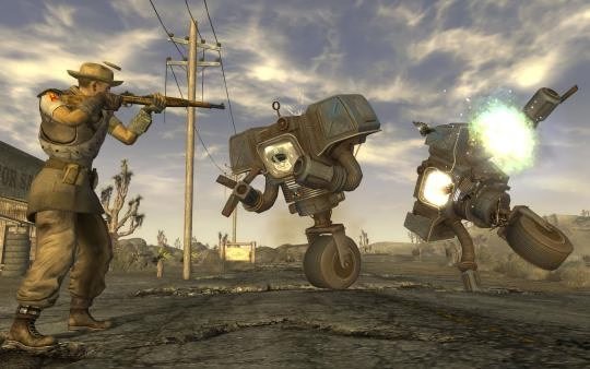 Screenshot from Fallout: New Vegas showing a character aiming a rifle at two robots on a deserted road under a cloudy sky.
