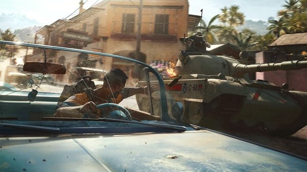 A screenshot from Far Cry® 6 showing a car chase with a man driving while a tank fires in a vibrant, tropical town setting.