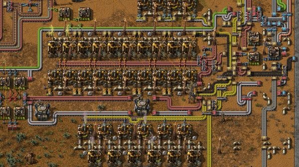 This Factorio screenshot displays a complex factory assembly line with conveyor belts, machines, and resources on a desert terrain.
