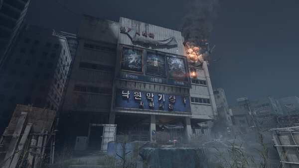 Screenshot from NAKWON: LAST PARADISE showing a dilapidated building with burning debris and fog in a post-apocalyptic setting.