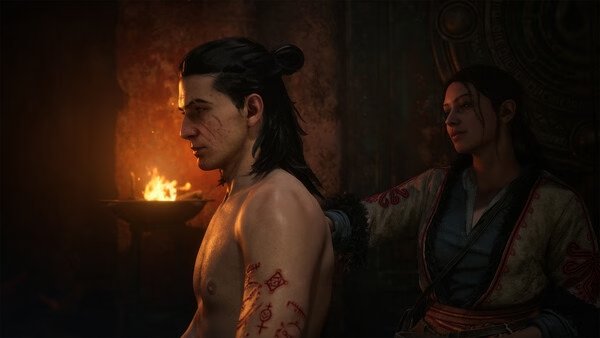 Screenshot from The Blood of Dawnwalker showing a tattooed man seated near a flame, with another character standing behind him.
