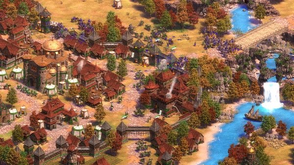 Screenshot from Age of Empires II showing a bustling medieval village, armies clashing, and a scenic river with a waterfall nearby.