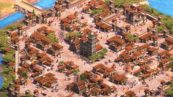 Age of Empires II screenshot featuring a bustling medieval city with stone buildings, walls, and a central tower surrounded by greenery.
