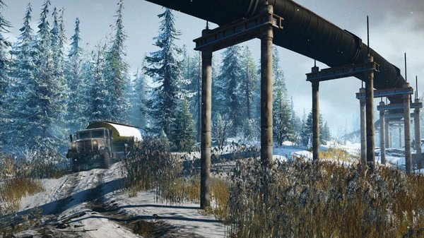 SnowRunner screenshot showing a truck navigating a snowy path beneath a large pipeline, surrounded by snow-covered trees.