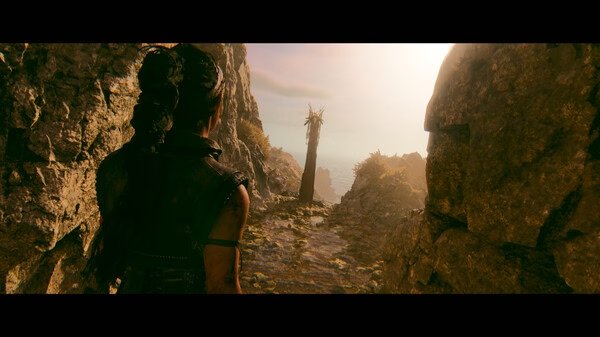 Screenshot from Hellblade II: Senua’s Saga showing Senua walking through a rocky path towards a distant, sunlit landscape.