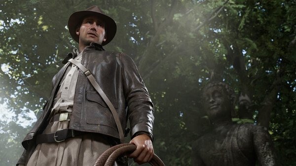 Screenshot from Indiana Jones and the Great Circle showing Indiana Jones holding a whip in a forest with a statue in the background.