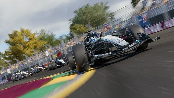 F1 25 screenshot: A race car speeds on a vibrant track, followed by other cars, with trees and spectators in the background.