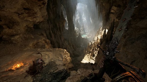 Screenshot from Fatekeeper: A warrior holding a large sword stands at the entrance of a vast, illuminated cavern with stalactites.