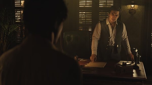 Screenshot from Mafia: The Old Country showing a tense meeting in a dimly lit office with two men discussing at a wooden desk.