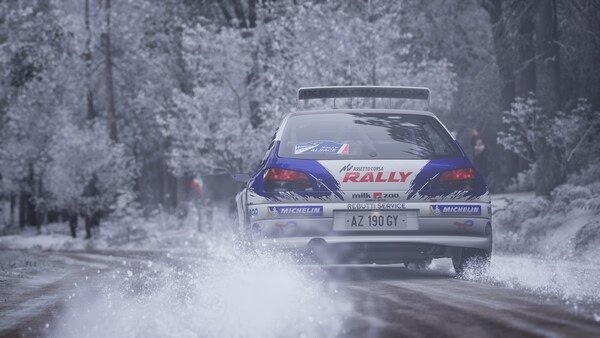 Screenshot from Assetto Corsa Rally shows a rally car speeding through a snowy forest track, kicking up snow behind it.