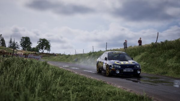 Assetto Corsa Rally screenshot: A rally car navigates a wet, narrow country road with spectators watching on a cloudy day.