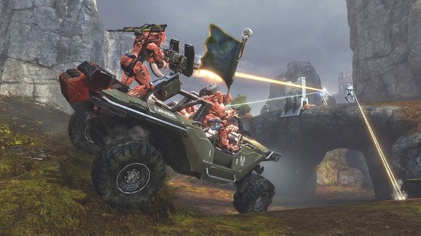 Screenshot from Halo: The Master Chief Collection showing armored soldiers driving a vehicle while engaged in a laser battle on rocky terrain.