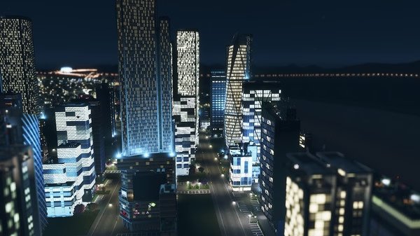 A nighttime screenshot from Cities: Skylines showing a brightly lit cityscape with modern skyscrapers and a river in the background.