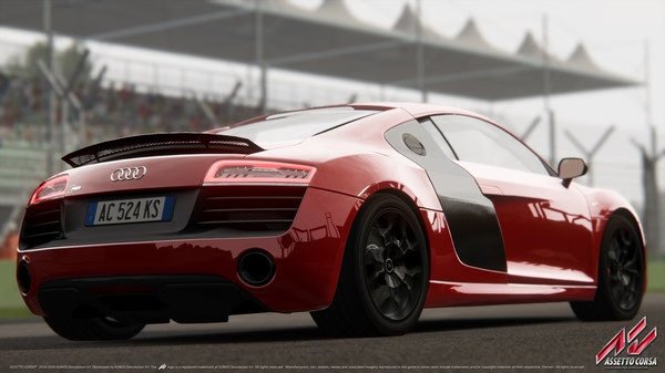 A red Audi R8 is parked on a racetrack in Assetto Corsa. The screenshot showcases its detailed design and realistic environment.