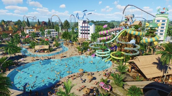 Screenshot from Planet Coaster 2 showing a lively water park with slides, pools, palm trees, and crowds enjoying a sunny day.