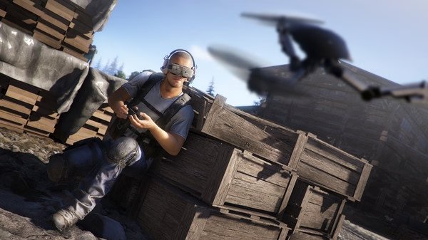 A screenshot from Tom Clancy's Ghost Recon Wildlands shows a soldier using a device, with a drone flying nearby in a wooden crate-filled area.
