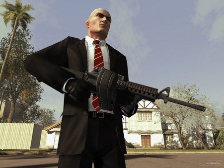 Hitman: Blood Money screenshot of Agent 47 holding a large weapon outdoors, wearing a suit and gloves, with houses in the background.