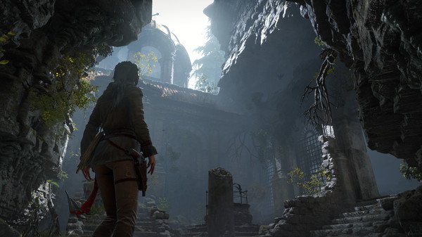 Screenshot from Rise of the Tomb Raider game showing a character exploring a shadowy, ancient stone ruin with overgrown foliage.