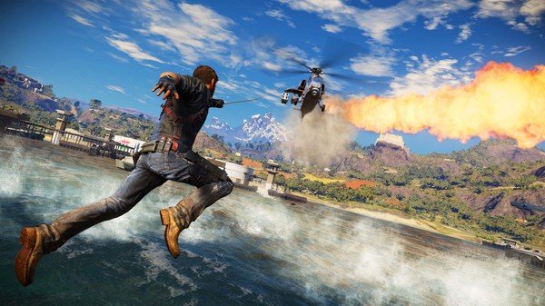 Just Cause 3 screenshot: A character uses a grappling hook to chase a helicopter shooting flames over a coastal area.