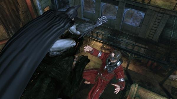Batman: Arkham Asylum screenshot showing Batman lunging at an enemy in red robes within a dimly lit industrial setting.
