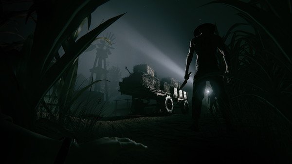 Outlast 2 screenshot: A shadowy figure holding a weapon approaches a cart loaded with hay under eerie moonlight in a dark rural setting.