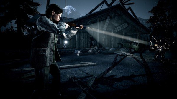 Alan Wake screenshot: A man shines a flashlight and points a shotgun in a dark, eerie setting with a wooden building in the background.