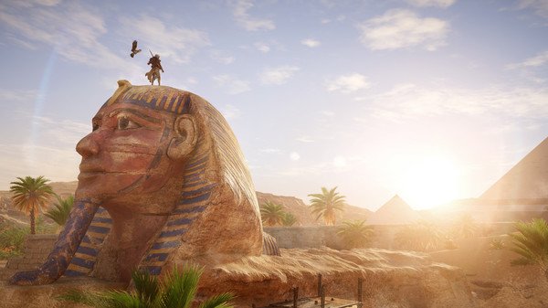 Screenshot from Assassin's Creed Origins showing a character standing on a giant Sphinx with pyramids in the background.