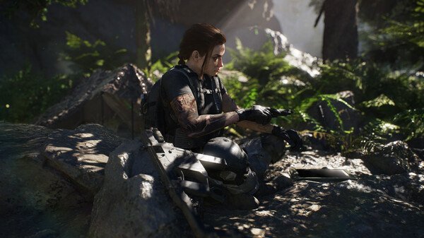 A character sits on a rock in a forest in Tom Clancy's Ghost Recon Breakpoint screenshot, wearing tactical gear.