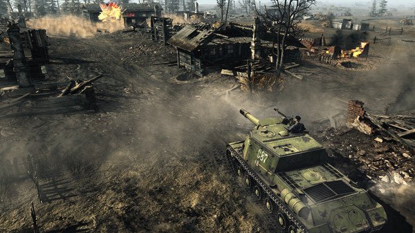Screenshot from Call to Arms - Gates of Hell: Ostfront showing a tank advancing through a war-torn village, surrounded by smoke and debris.
