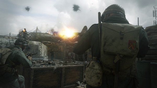 A Call of Duty: WWII screenshot showing soldiers in combat near sandbags as a plane crashes in the background.